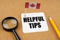 On the table is the flag of Canada, a pencil, a magnifying glass and a sheet of paper with the inscription -Helpful Tips