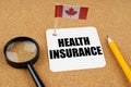 On the table is the flag of Canada, a pencil and a sheet of paper with the inscription - Health insurance