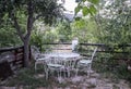 table and four white wrought-iron chairs on a terrace overlooking the countryside with many trees and vegetation