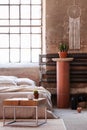 Table in front of a bed, stand with a plant and iron radiator in an industrial bedroom interior Royalty Free Stock Photo