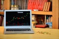 On the table golden bitcoins and laptop with stock exchange graph on screen, blurred shelf with books in the background