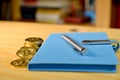 On the table golden cryptocurrency coins, blue notebook with pen, blurred shelf with books in the background