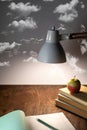 table lamp illuminates the workplace on the office desk, stack of books, an open notebook, a pencil and an apple on a gray Royalty Free Stock Photo