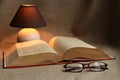 Table lamp, old book with yellowed pages and glasses