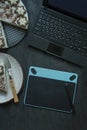 On the table is a laptop, graphics tablet, cake and a cup of coffee. Office supplies. Working environment. View from above. Dark