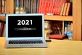 On the table laptop with text - 2021 loading - on screen, blurred shelf with books in the background