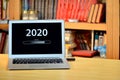 On the table laptop with text - 2020 loading - on screen, blurred shelf with books in the background