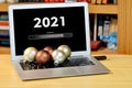 On the table laptop with text - 2021 loading - on screen and with christmas decorations on the keyboard, blurred shelf with books