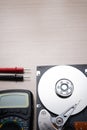 On the table lies an opened old hard drive and a multimeter for checking and repairing it