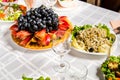 Table lined with variety of dishes from which the centerpiece is dish with sliced fruit
