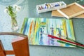 Table with a lying oil painting on canvas, box of paints in tubes, brushes and bouquet of fluffy dandelions. Romantic