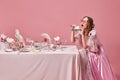 Portrait of beautiful, hungry, blond princess wearing fancy pink dress and sunglasses eating sandwich over studio