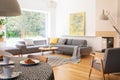 Table next to armchair in white home interior with grey settee and yellow painting. Real photo