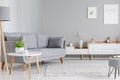 Table next to grey sofa in scandi living room interior with post