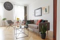 Table next to settee and plant in living room interior with grey armchairs and posters. Real photo Royalty Free Stock Photo