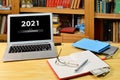 On the table notebook, eyeglases and laptop with text - 2021 loading - on screen, blurred shelf with books in the background