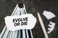 On the table is a notebook on which lies a piece of torn paper with the inscription - Evolve Or Die Royalty Free Stock Photo