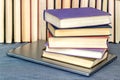 On the table are a number of books and a gray laptop under a pile of books