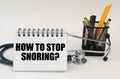 On the table are office supplies, a stethoscope and a notepad with the inscription - How to stop snoring