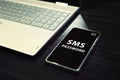 Table with open laptop and black-screened smartphone with white written words SMS password on its display. Concept of Royalty Free Stock Photo