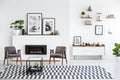 Table on patterned carpet in white living room interior with grey armchairs and posters. Real photo Royalty Free Stock Photo