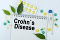 On the table are pills, a thermometer, leaves and a notebook with the inscription -Crohns Disease