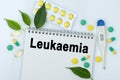 On the table are pills, a thermometer, leaves and a notebook with the inscription -Leukaemia