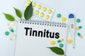 On the table are pills, a thermometer, leaves and a notebook with the inscription -Tinnitus