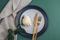 Table place setting with white rose flower, plates and golden cutlery on dark green background. Top view, flat lay Royalty Free Stock Photo