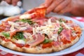 on table plate with round italian pizza cut into slices, male hands take pieces of pizza with salami, cheese, arugula, hands with Royalty Free Stock Photo