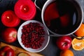 On the table is a pot of compote, apples and oranges, a bowl of cranberries and burning red candles.