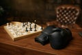 Table in room with boxer gloves and chessboard with chesspieces, chess conflict Royalty Free Stock Photo