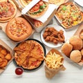 Table scene with large variety of take out and fast foods. Hamburgers, pizza, fried chicken and sides. Top view on a white wood