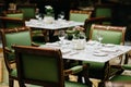 Table served with luxury glasses, cutlery, flowers, green chairs around in cozy restaurant. Nobody in shot. Decorated table for Royalty Free Stock Photo