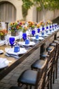 Table setting for a wedding celebration in an outdoor mission style patio with blue and orange theme, and flower decorations Royalty Free Stock Photo