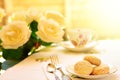 Table set with vintage bone china tea set, sesame biscuits on saucer and white roses on a bright sunny day in the garden