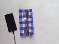 Table setting on a blue and white gingham napkin with a cellphone charging on a white wooden table