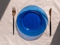 Table setting empty blue glass plate with fork knife on linen cloth top view daylight harsh shadows. Festive dish place Royalty Free Stock Photo
