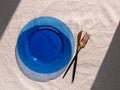 Table setting empty blue glass plate with fork knife on linen cloth top view daylight harsh shadows. Festive dish place Royalty Free Stock Photo