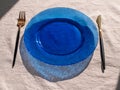 Table setting empty blue glass plate with fork knife on linen cloth top view daylight harsh shadows. Festive dish place Royalty Free Stock Photo