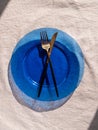 Table setting empty blue glass plate with fork knife on linen cloth top view daylight harsh shadows. Festive dish place Royalty Free Stock Photo