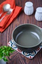 Table setting, empty olive green ceramic bowl on a colored stand, orange napkin, cutlery, salt and pepper shaker