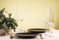 Table setting for a festive dinner for two, black plate and glasses with flower arrangement on yellow background Royalty Free Stock Photo