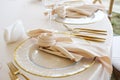 Elegant table setting with gold cutlery, glassware, and folded napkins on white tablecloth, featuring clear plates with gold rims Royalty Free Stock Photo