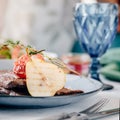 Table setting in restaurant is fresh meat steak with pear and tomato decoration. Cutlery and wine glass Royalty Free Stock Photo