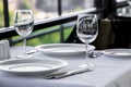 Table setting in restaurant terrace with green background. Empty wine glasses, plates, forks, knifes on the tablecloth