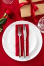 Table setting for Valentines Day romantic dinner. Top view fork and knife on red napkin on plate, rose flower, gift box, glasses