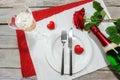 Table setting for a Valentines dinner, red rose and two hearts, chapagne glass and bottle around a white plate on napkins and on a Royalty Free Stock Photo