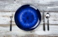 Table setting with vintage cutlery, empty blue plate, fork, spoon and knife on white rustic wood table Royalty Free Stock Photo