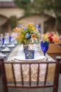 Table setting for a wedding celebration in an outdoor mission style patio with blue and orange theme, and flower decorations Royalty Free Stock Photo